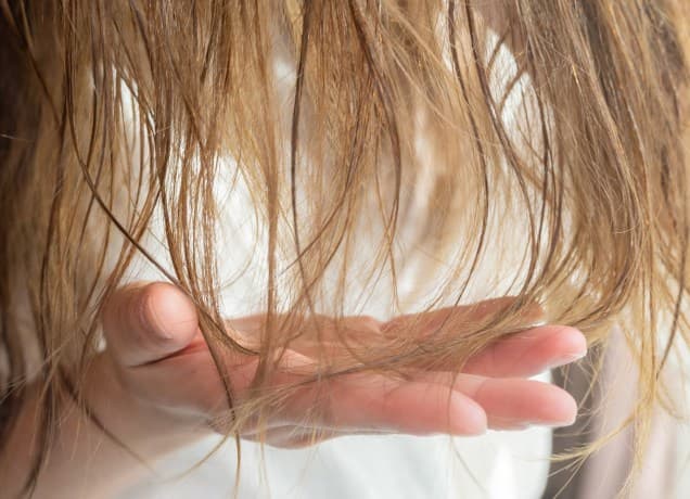 things to stop doing if you have thin hair universal: a closeup image of a woman examining her blonde hair