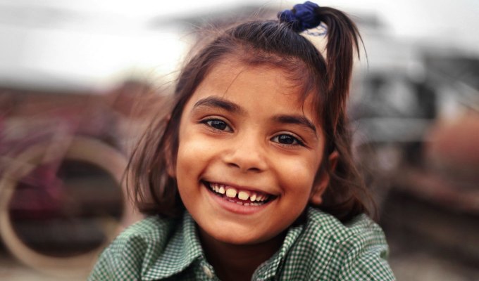 baby-names-that-mean-love: Cheerful little girl laughing portrait close up. She seems to be of South Asian descent. She's wearing her hair in a half up/half down style and wears a green and white checkered shirt.