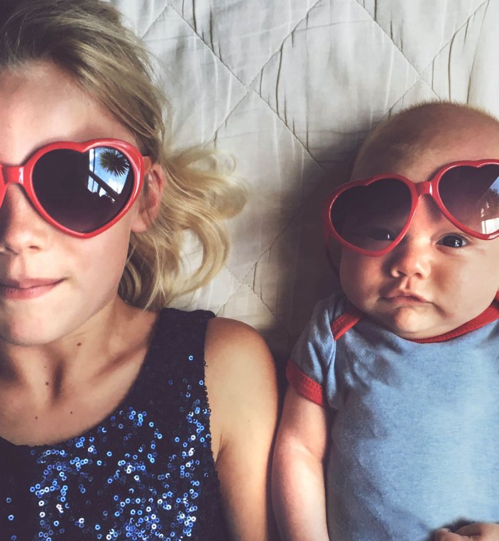 baby-names-that-mean-love: Young girl laying beside baby brother both wearing red love heart glasses.