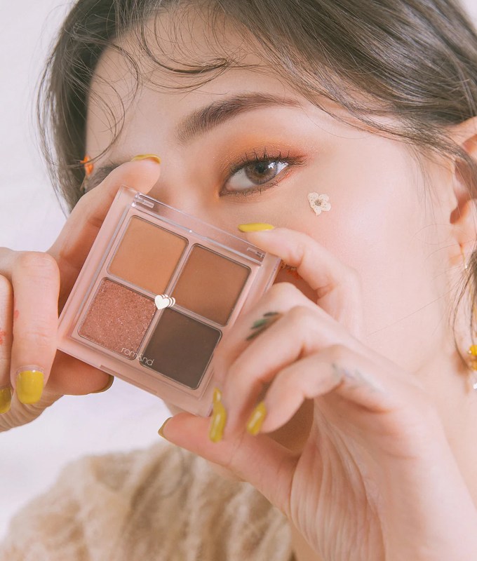 best korean makeup brands rom&nd: a woman holding an eyeshadow palette against her face