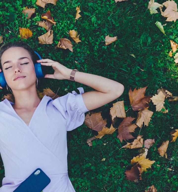 best-songs-for-fall: a woman laying on brown leaves and wearing headphones.