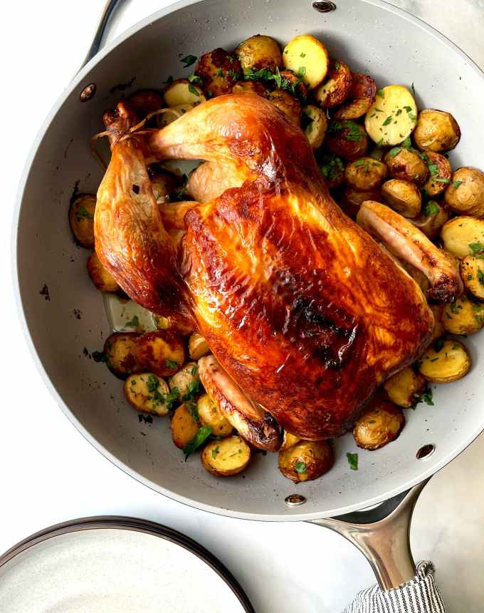 best big-batch recipes: whole roast chicken in a skillet next to potatoes cooked in chicken fat