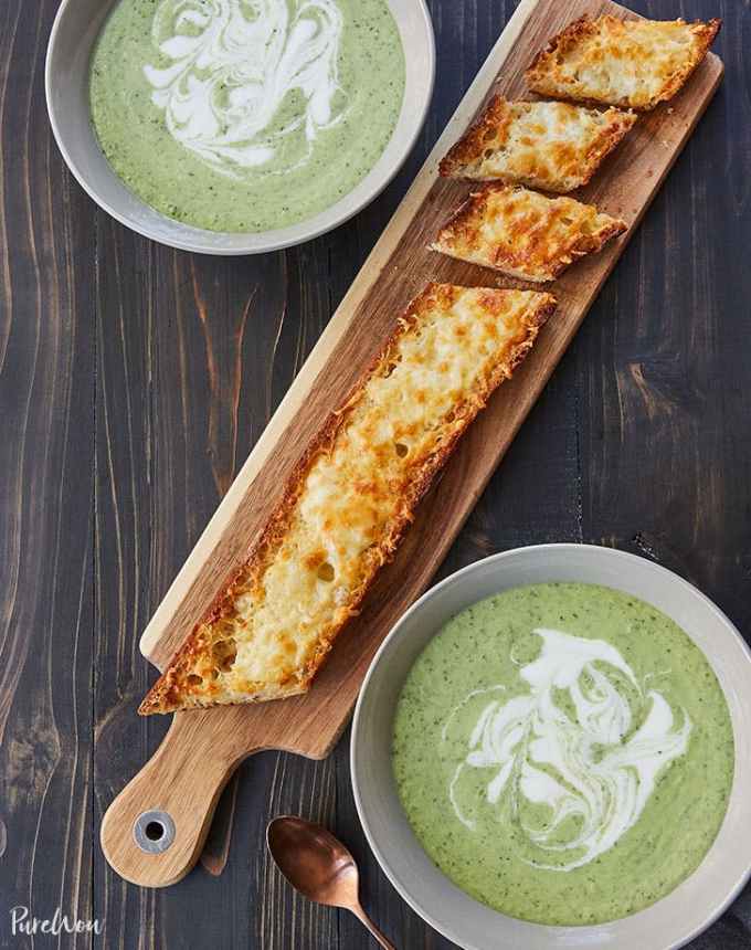 easy lunch ideas: aerial of asiago-crusted baguette on cutting board between two bowls of 15-minute cucumber-avocado blender soup