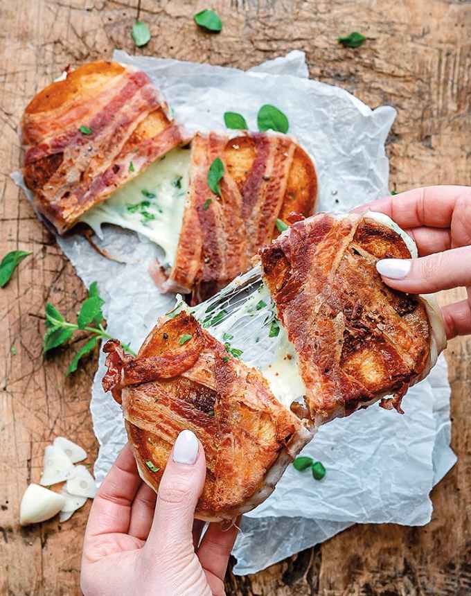 easy lunch ideas: two pancetta-wrapped grilled cheese sandwiches, one on a piece of parchment and the other being pulled apart by two hands