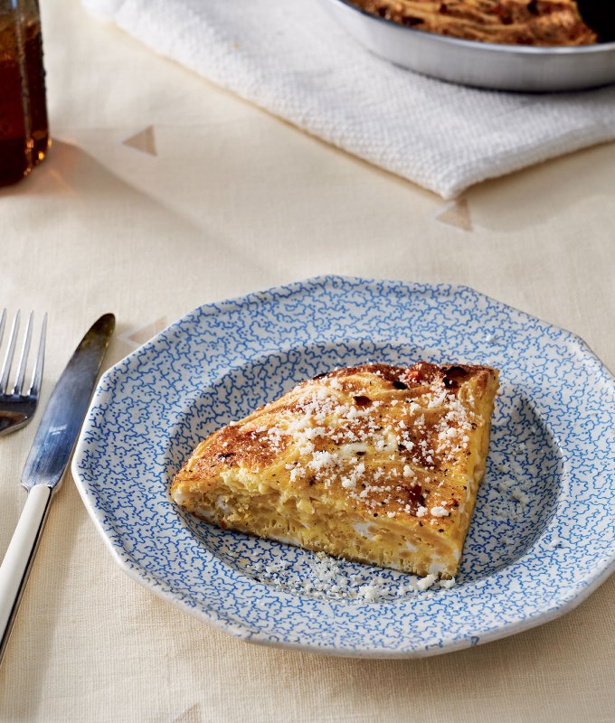 leftover pasta frittata recipe: a blue plate with a quarter of a leftover pasta frittata on it, next to a fork and knife