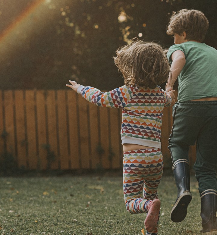 Three siblings, being led by middle child, run toward a rainbow.