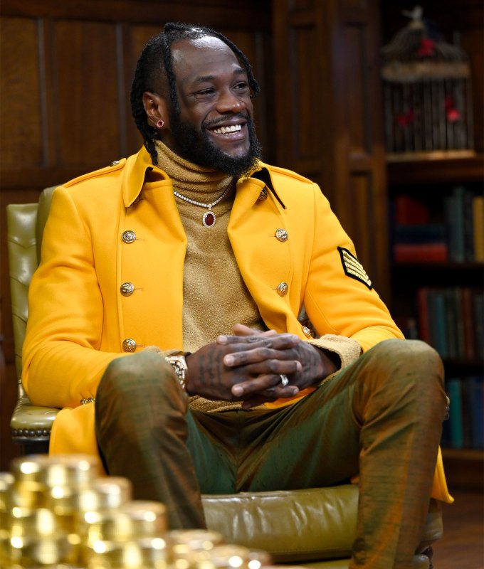 the-traitors-season-2-cast-ranked: A photo of Deontay Wilder sitting down. He wears a yellow jacket, beige top and green pants.