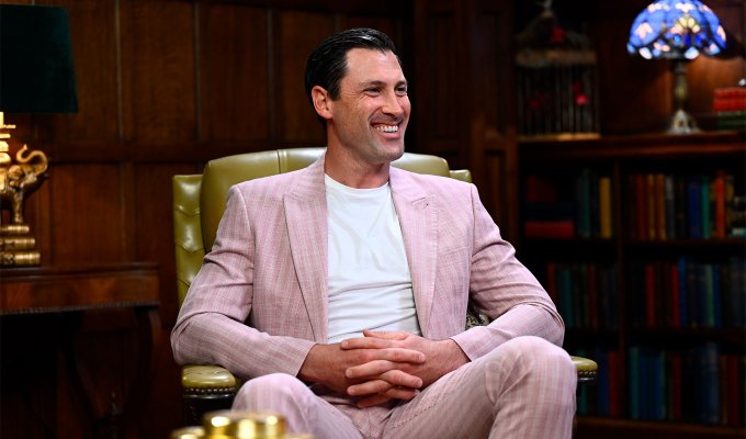 the-traitors-season-2-cast-ranked: A photo of Maksim-Chmerkovskiy sitting in a chair. He wears a pink suit.