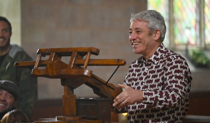 the-traitors-season-2-cast-ranked: A photo of John Bercow next to a crossbow in a patterned top.