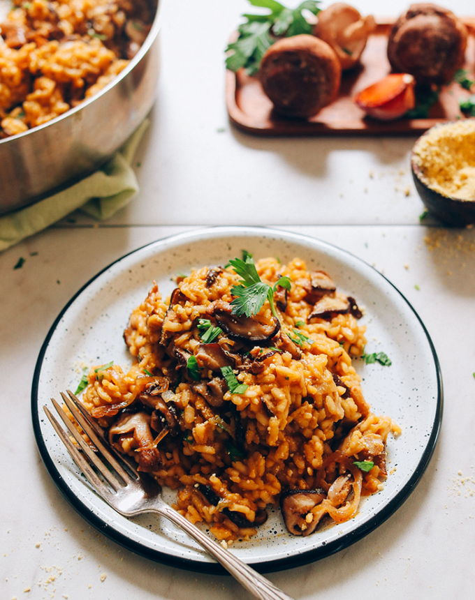 best big-batch recipes: caramelized shiitake mushroom risotto on a plate, with vegetables and a baking dish of the risotto in the background