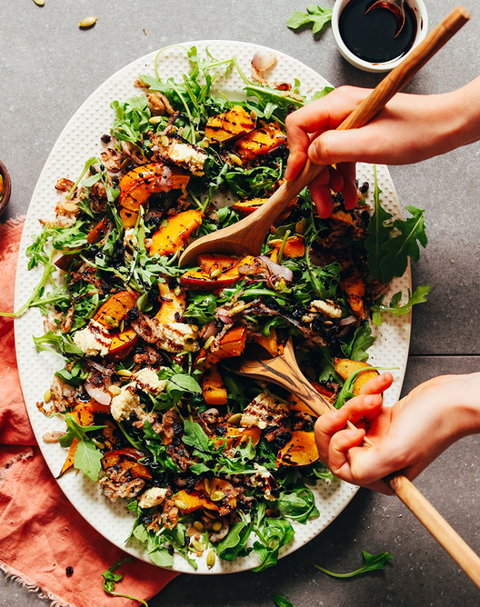 best big-batch recipes: person using salad tongs to scoop roasted squash salad with shallots and balsamic reduction